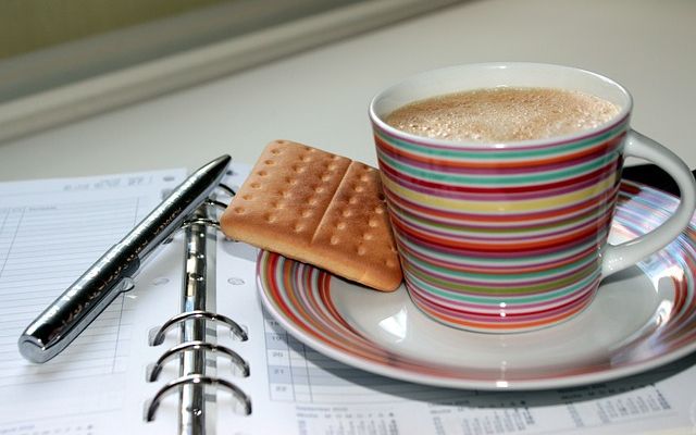 A cup of coffee, a biscuit and an open diary planner.